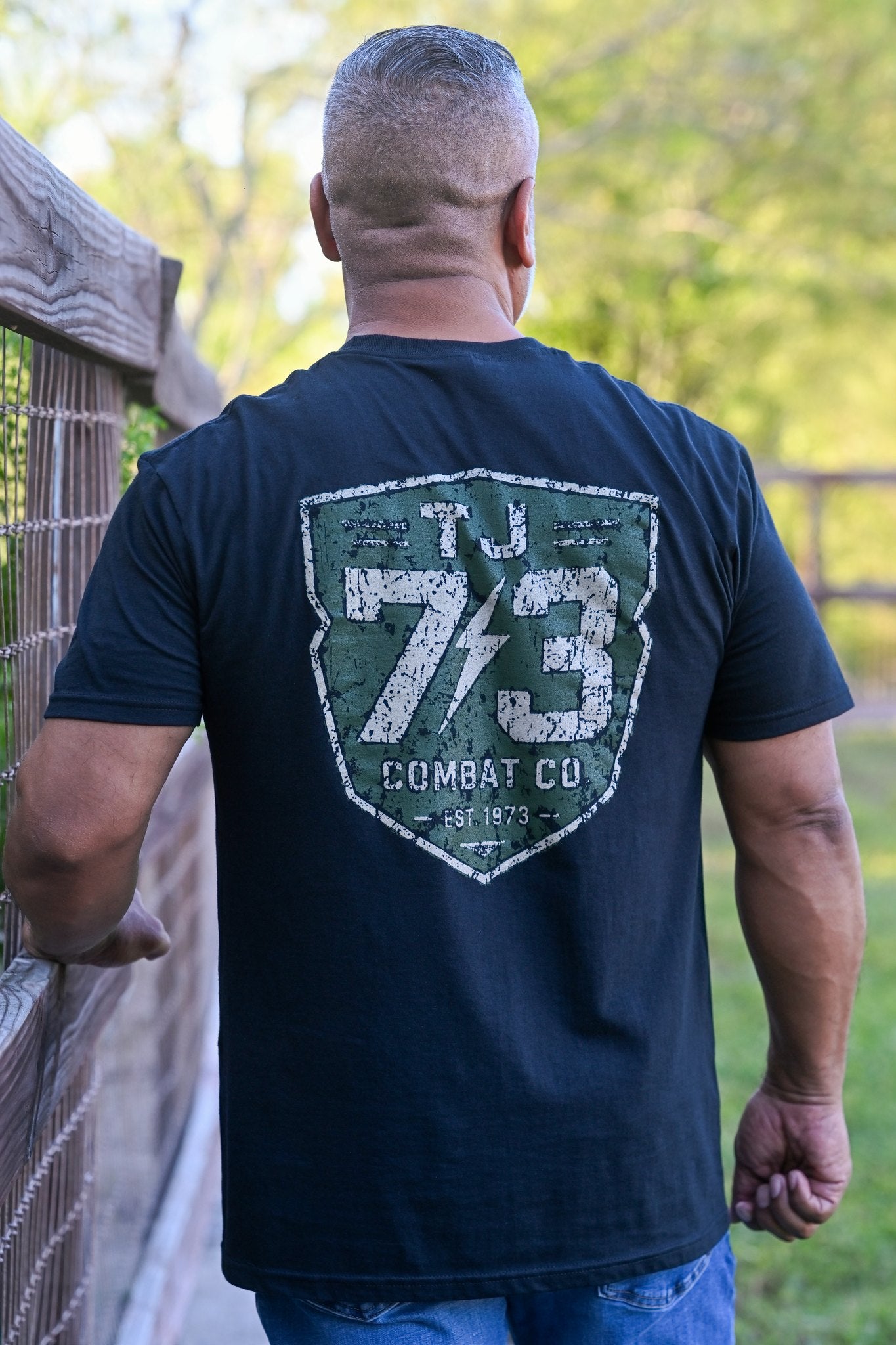 Man wearing TJ73 Combat Co. black tee, back view outdoors