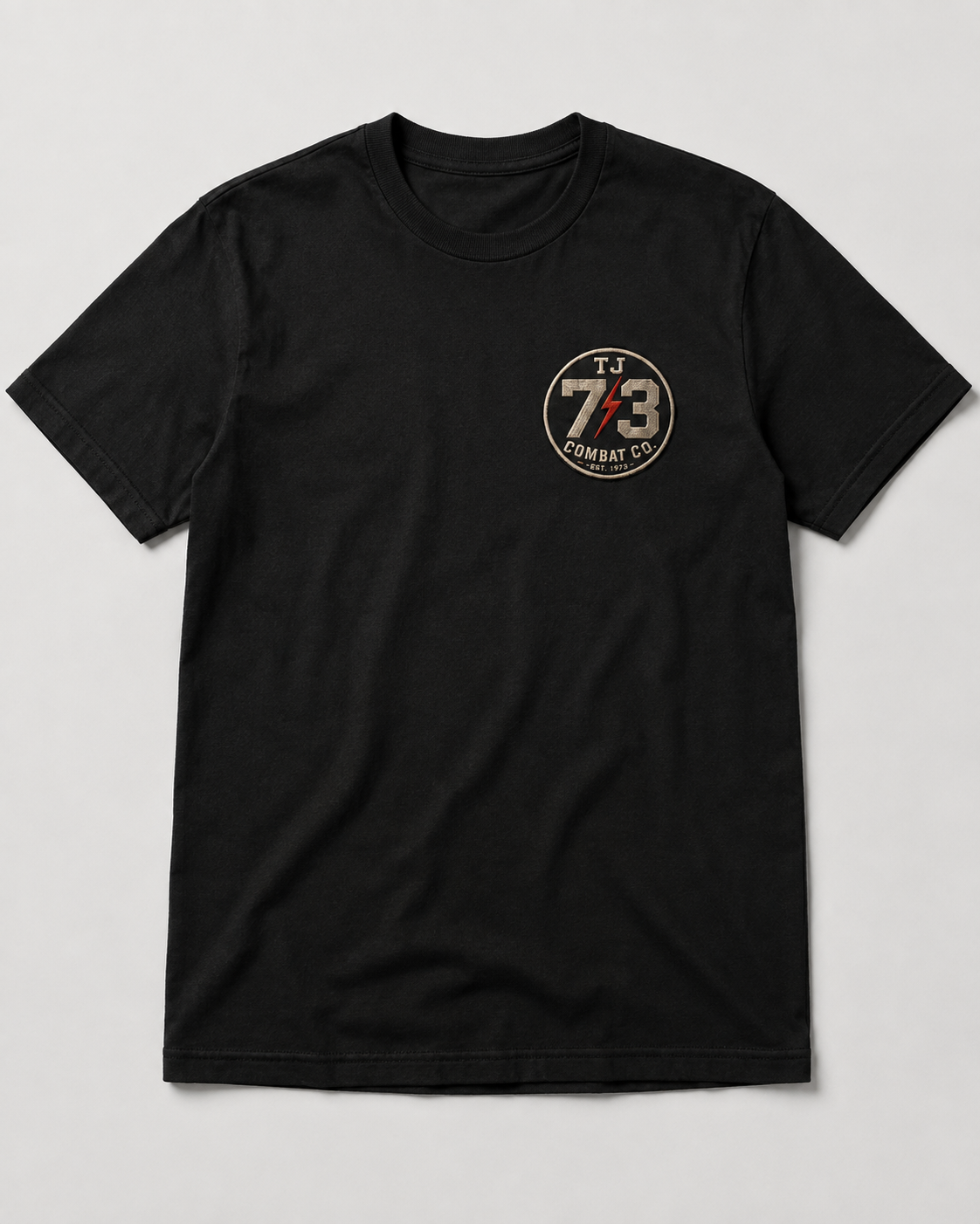 TJ73 Combat Company Tee, front — black AS Colour Staple tee with TJ73 circle patch on left chest